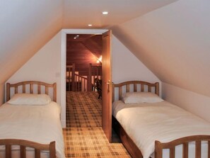 A narrow, sloped room with two wooden beds, a checkered floor, and a wooden staircase leading to an upper level.