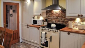 Una cocina con armarios blancos, estufa, microondas y hervidor.