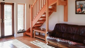 Una escalera de madera que lleva a un nivel superior, un sofá de cuero marrón y un cuadro de un ciervo en la pared.