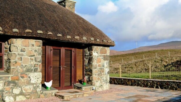 Una casa de piedra con techo de paja, contraventanas de madera y chimenea de piedra.