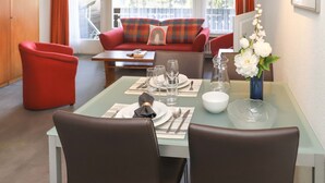 A dining area with a glass table, two red chairs, a sofa with colorful cushions, and a vase with white flowers. - Matten (Utoring) by Interhome (Zermatt)