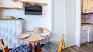 A compact living space with a dining table set for four, a television mounted on the wall, and a kitchenette with cabinets and a refrigerator. - Chavière 832 by Interhome (Les Menuires)