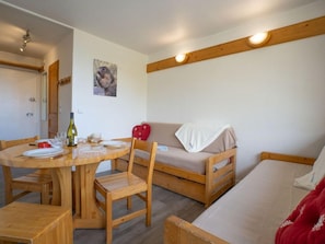 Une pièce chaleureuse avec une table à manger en bois, préparée pour un dîner à deux, un canapé et un lit.