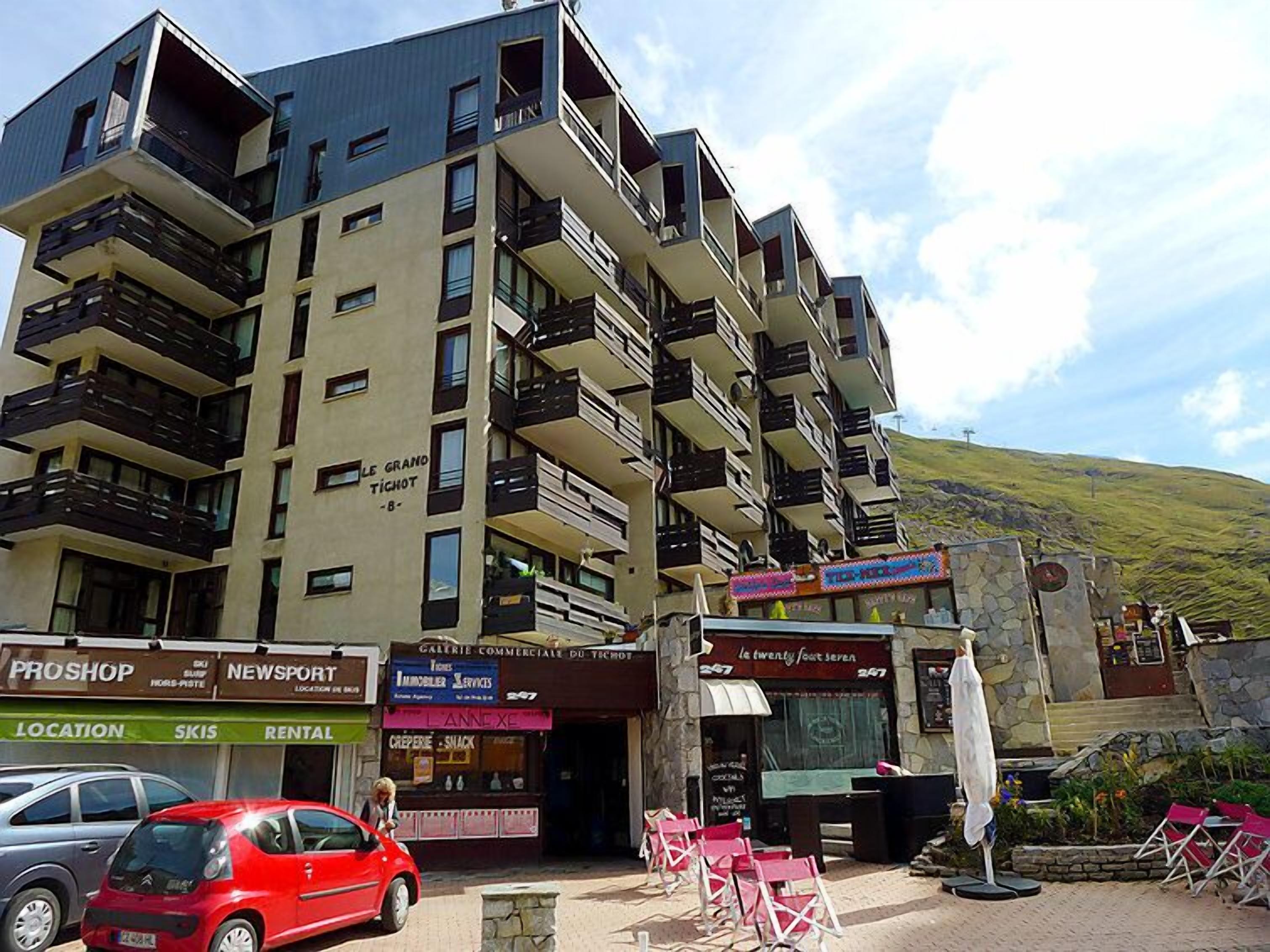 A multi-story building with balconies, a visible restaurant sign, and a car parked in front.