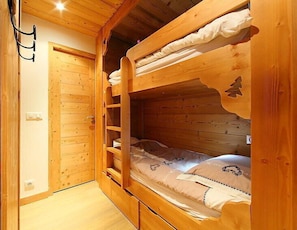 A wooden bunk bed room with a wooden door and a small shelf.
