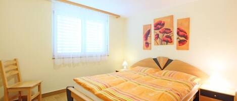 Une chambre à coucher comprenant un lit, une chaise, une table de chevet et une fenêtre avec des stores.