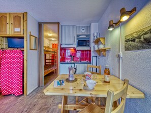 Una cocina compacta con microondas, lavamanos y armarios de madera. En primer plano, una mesa de comedor con sillas.
