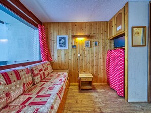 Una habitación acogedora con una pared de madera, un sofá con un estampado llamativo, una pequeña mesa de madera y un televisor fijado a la pared.