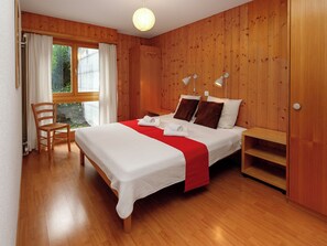 Ein Schlafzimmer mit Holzwänden, einem Bett, Nachttischlampen, einem Sessel und einem Fenster mit Vorhängen.