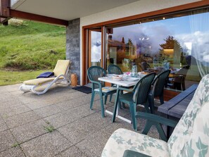 A patio with a table and chairs, a sun lounger, and a view of a mountain. - Fénestral R01 by Interhome (Ovronnaz)