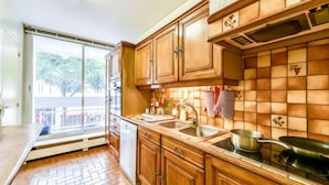Una cocina con armarios de madera, un lavamanos de acero inoxidable y una ventana con vistas a un balcón.