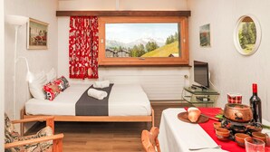 Ein gemütliches Schlafzimmer mit Bett, Fernseher und Essbereich mit Tisch für zwei Personen.