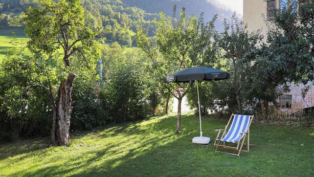 Un giardino con prato, una sedia di legno e un ombrello nero.