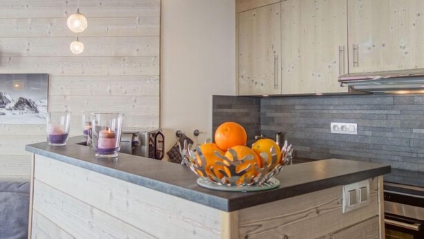 Een moderne keuken met houten kastjes, een zwart aanrecht en een fruitschaal met sinaasappels.