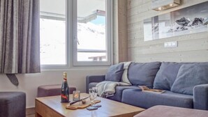 Een gezellige woonkamer met een grijze bank, een houten salontafel en een raam met gordijnen.