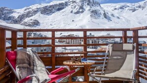 Een houten terras met een tafel en stoelen met uitzicht op een besneeuwd berglandschap.