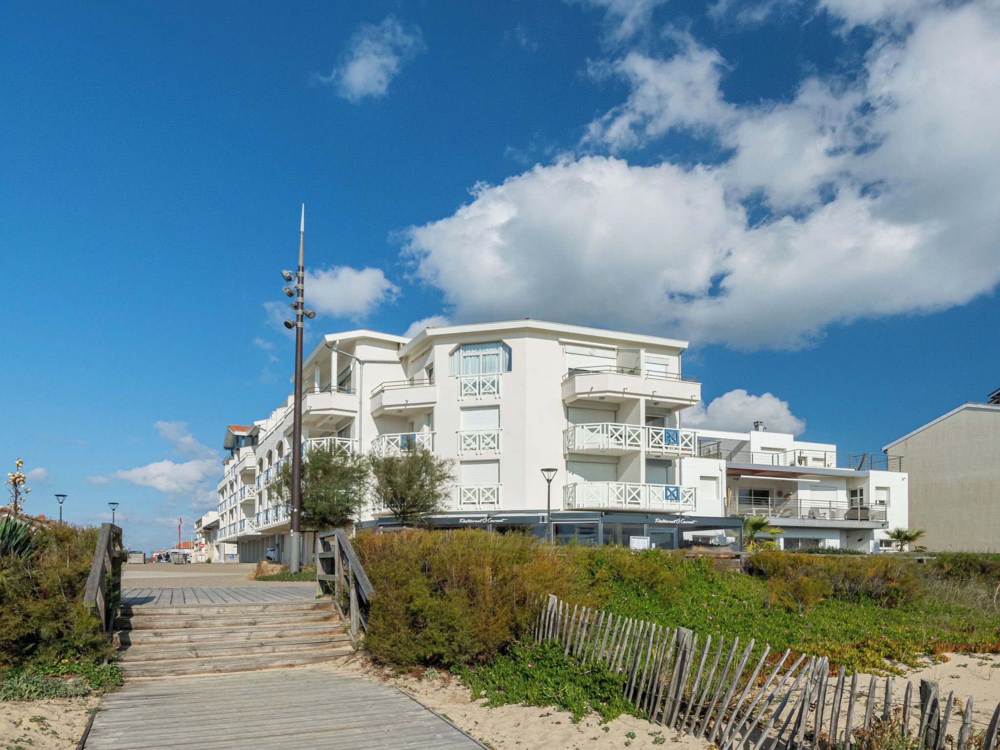 Ein Hotel an der Küste mit einem hölzernen Steg, der zum Eingang führt, mit mehreren Balkonen und blauem Himmel.