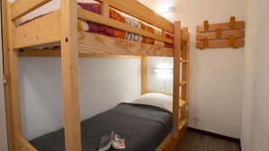 Habitación con literas de madera, una mesita pequeña y un estante fijado a la pared.