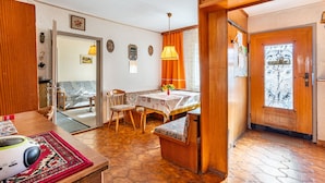 Uma sala de jantar acolhedora com mesa de madeira, cadeiras e um banco. Há um tapete estampado no chão e um candeeiro no teto.