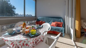 Ein Balkon mit Frühstückstisch, einer Couch mit Kissen und Blick auf Bäume und Gebäude.
