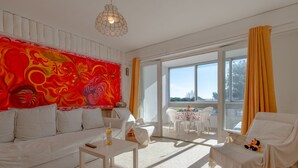 Ein modernes Wohnzimmer mit einem weißen Sofa, einem kleinen Tisch und Ausblick ins Freie durch große Fenster.