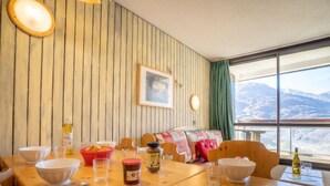 A wooden dining table with bowls, glasses, and condiments in a room with wooden paneling and a mountain view.
