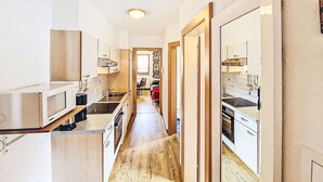 Une cuisine étroite avec un plancher en bois, des armoires blanches et un four à micro-ondes.