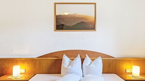 Un lit bien fait, avec du linge de lit blanc et des oreillers, une tête de lit en bois, des lampes de chevet et un tableau représentant un paysage, accroché au mur.