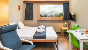 Une chambre d’hôtel avec un lit, un bureau, une chaise et une fenêtre donnant sur la montagne.