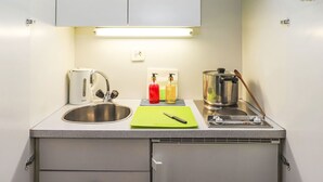 Une cuisine compacte équipée d’un évier en acier inoxydable, d’une bouilloire, d’une planche à découper et d’une autre bouilloire posée sur le comptoir.