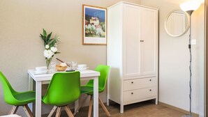 Un coin repas avec une table blanche, des chaises vertes, un buffet blanc et un tableau encadré au mur.