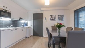A modern kitchen with white cabinets, a built-in oven, and a dining area with a table and chairs.