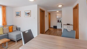 Una sala de estar moderna con un sofá, una mesa de comedor y sillas. Se observa una zona de cocina al fondo, con una cafetera y armarios.