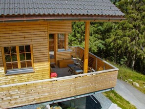 Una cabaña de madera con balcón, ventanas grandes y vistas al bosque circundante.