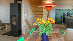 Un intérieur en bois comprenant une table à manger, des chaises, un vase de tulipes, un luminaire suspendu et un coin cuisine.