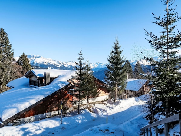 Un albergue cubierto de nieve con fachada de madera, rodeado de árboles cargados de nieve y montañas nevadas al fondo.