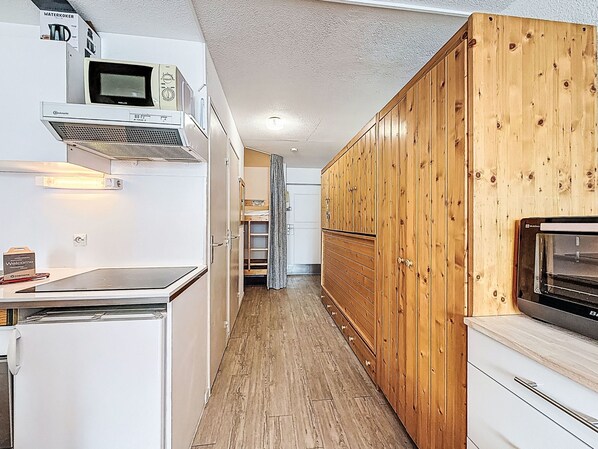 A narrow kitchen with white appliances, wooden cabinets, and a built-in microwave.