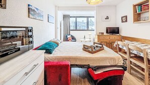 Ein gemütlicher Raum mit Bett, Schreibtisch, Fernseher und einem Fenster mit Blick auf Gebäude.
