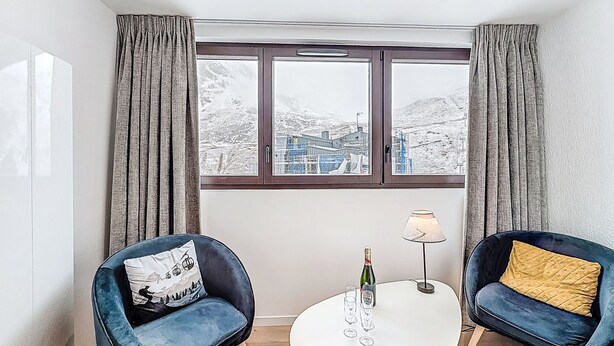Ein stilvolles Zimmer mit zwei blauen Sesseln, einem weißen Tisch und Blick auf eine verschneite Landschaft durch große Fenster.