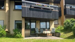 Ein zweistöckiges Gebäude mit einem Balkon, einer Außenbereich-Sitzgelegenheit mit Stühlen und Tisch sowie einem kleinen Garten.