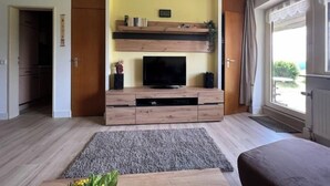 Ein modernes Wohnzimmer mit Flachbildfernseher, Holzunterhaltungseinheit und großem Fenster mit Blick ins Freie.