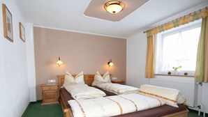 A double bed with a wooden frame and a brown mattress, two bedside tables, two wall-mounted lamps, a window with curtains, and a radiator. - Apartment Fabian by Interhome (Kaltenbach)