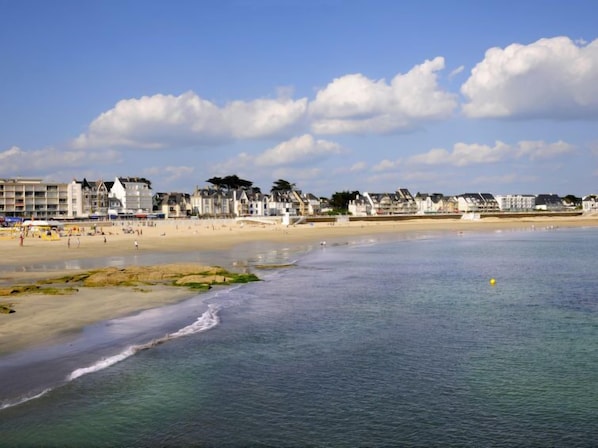 A coastal beach with buildings along the shore, a sandy beach, and calm water.