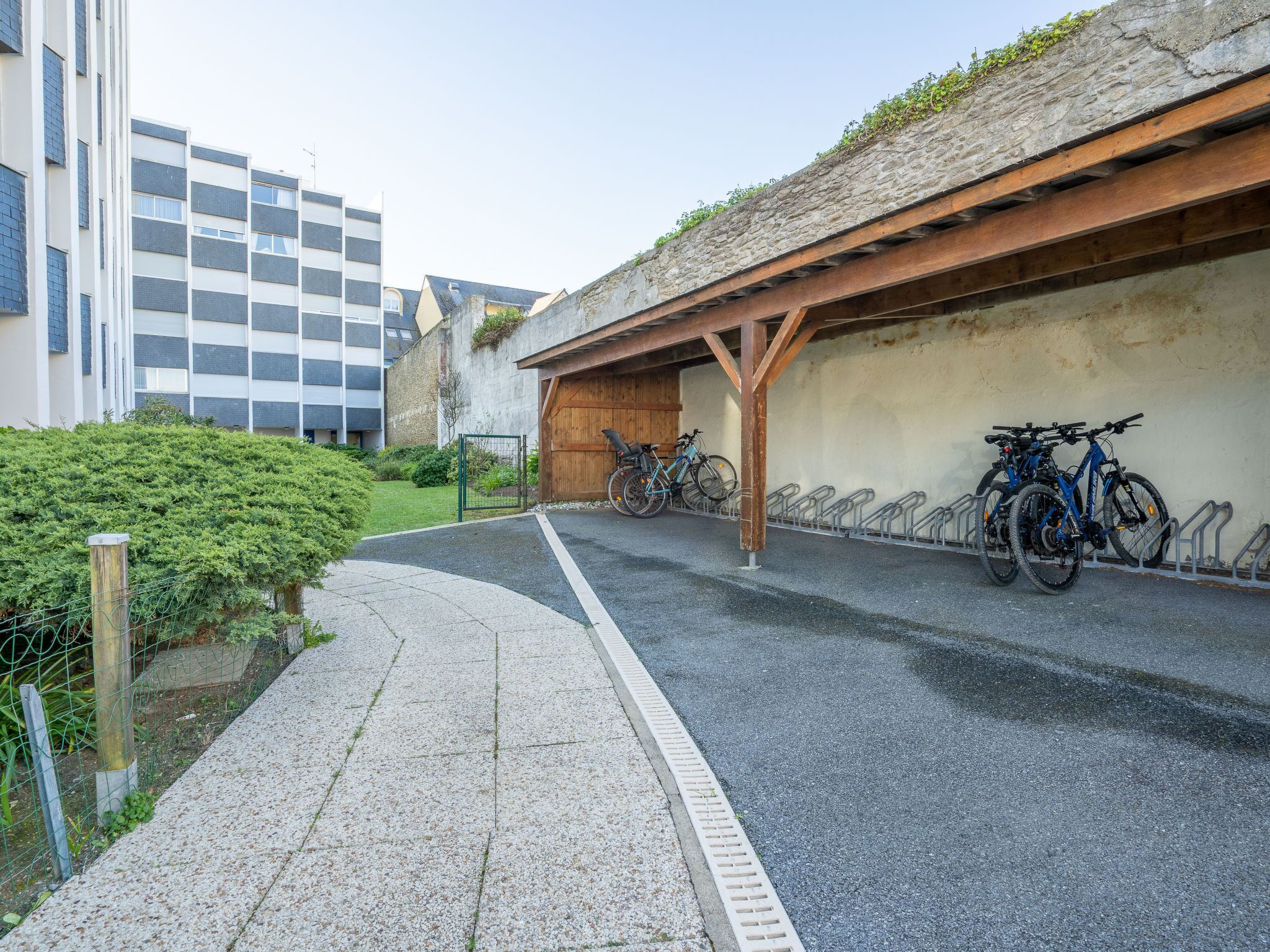 Uma área de estacionamento coberta para bicicletas com um caminho de cascalho que leva a um edifício.