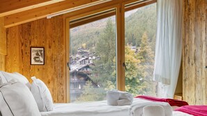 A hotel room with two beds, a large window with a view of a village, wooden walls, and a framed picture on the wall. - Rütschi by Interhome (Zermatt)