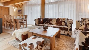 A cozy living room with a wooden ceiling, a sofa with cowhide cushions, a wooden coffee table, and a dining area with wooden chairs and a table. - Rütschi by Interhome (Zermatt)