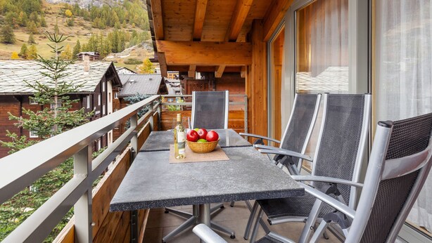 A balcony with a table, chairs, and a basket of apples and a bottle. - Rütschi by Interhome (Zermatt)