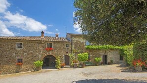 Un bâtiment en pierre doté d’une cour intérieure, avec un chemin de gravier et des plantes en pot.