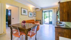 Een eethoek met een houten tafel en stoelen, een bank, en uitzicht op de omgeving door een glazen deur.
