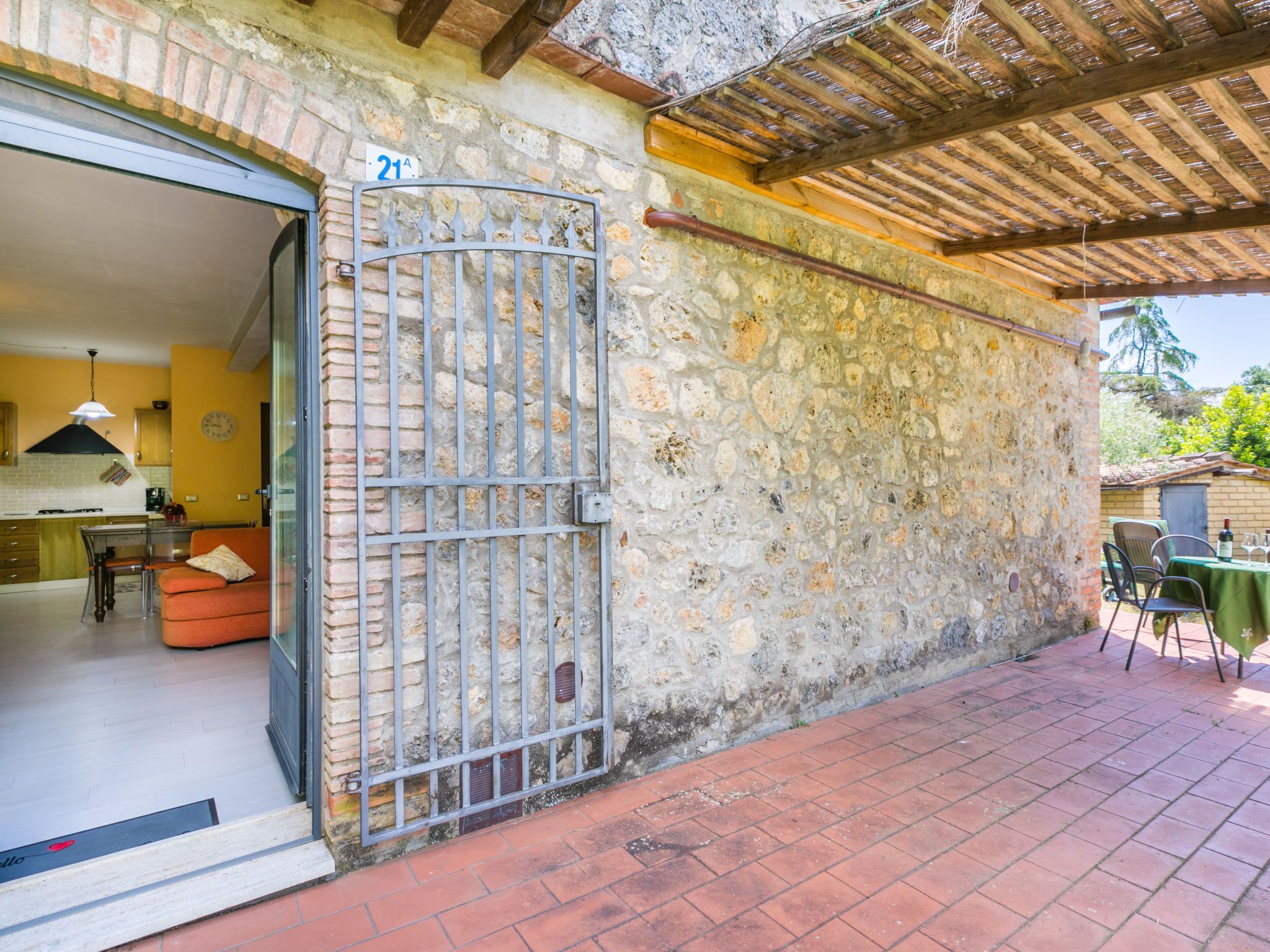 Een stenen gebouw met een metalen poort, een zichtbare keuken en een patio met een tafel en stoelen.